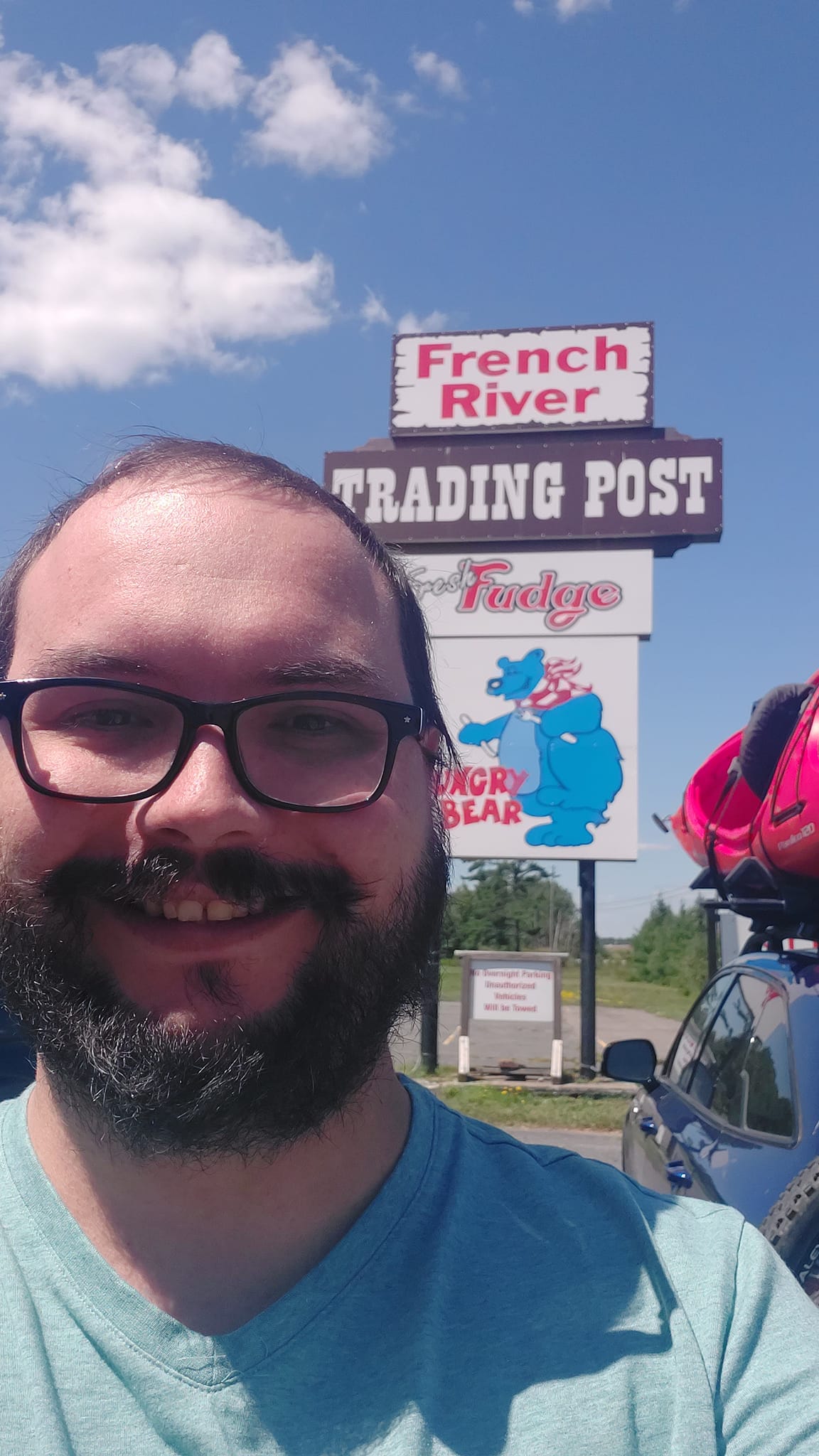 A man short hair and facial hair stands in front of a building with a sign that says French River Trading Post